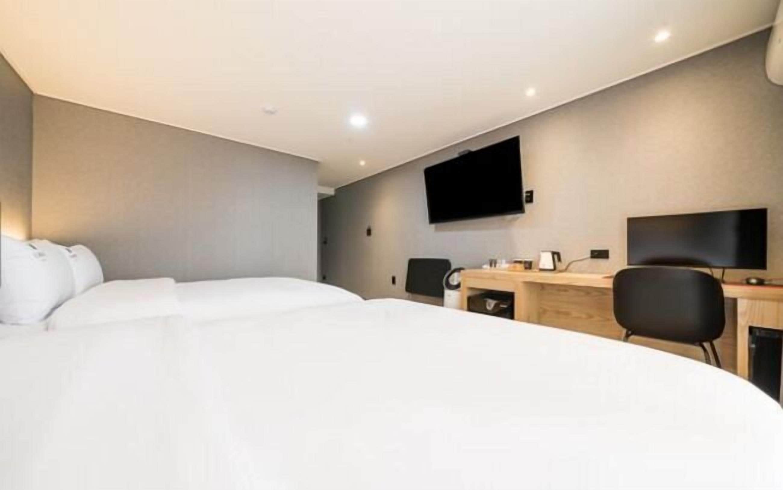 Een moderne hotelkamer met een groot bed, een bureau, een stoel, een flatscreen-televisie aan de muur en een klein tafeltje met een lamp.