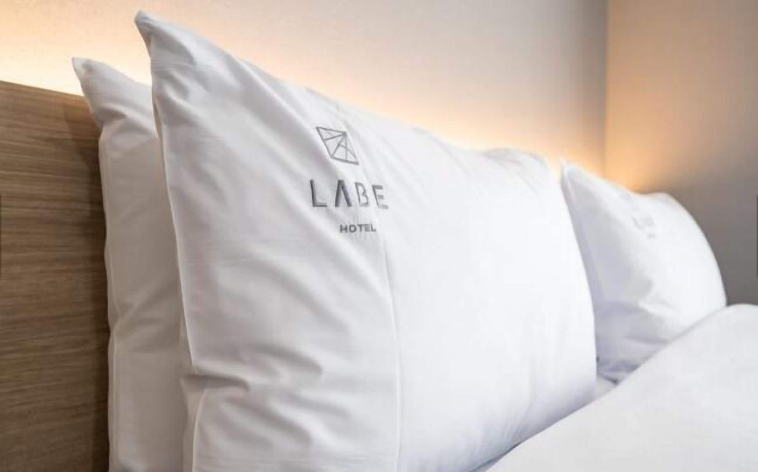 Letto d'albergo con cuscini bianchi e il logo dell'Hotel Labe.