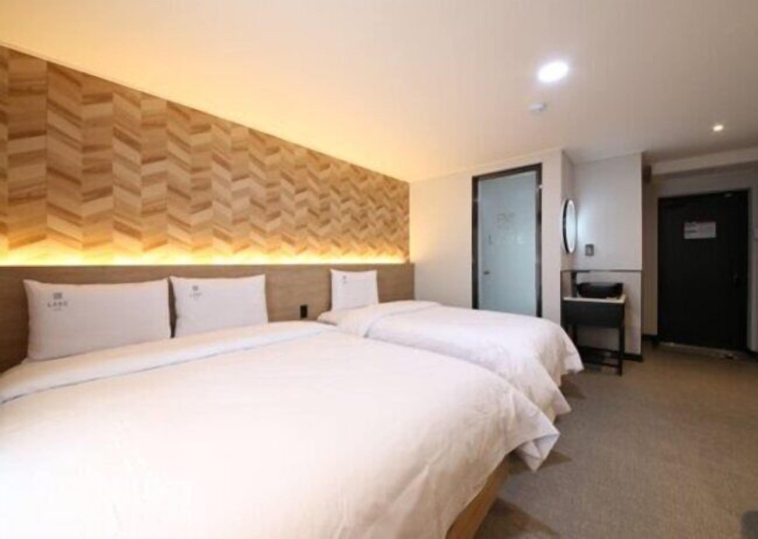A hotel room with two beds, a wooden headboard, a desk, and a door.