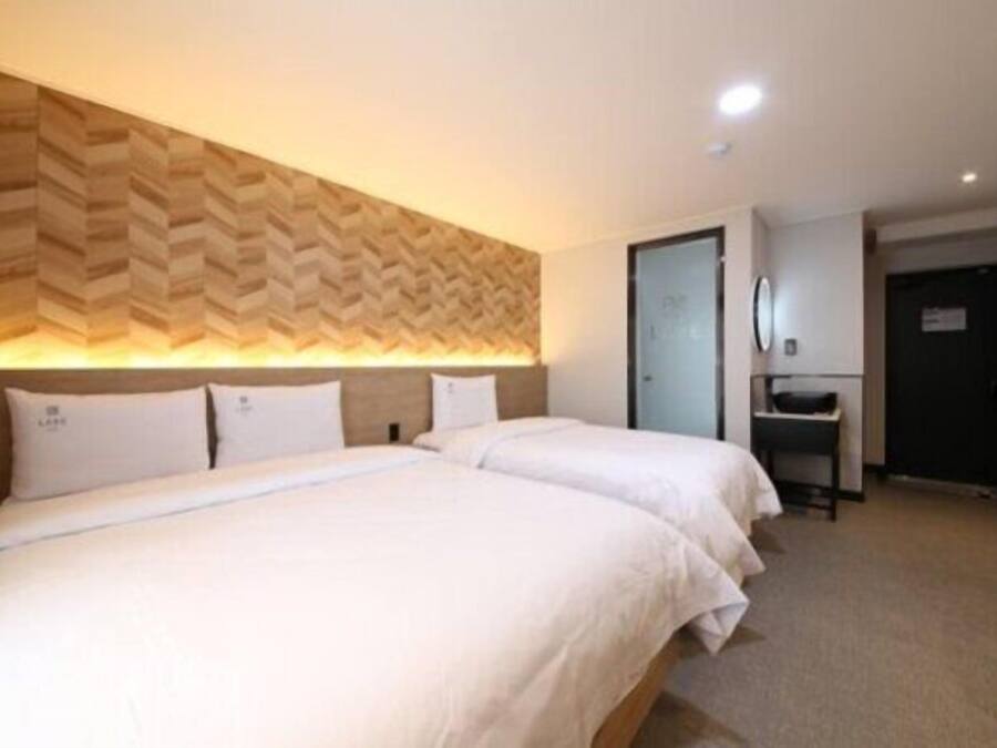 A hotel room with two beds, a wooden headboard, a desk, and a door.