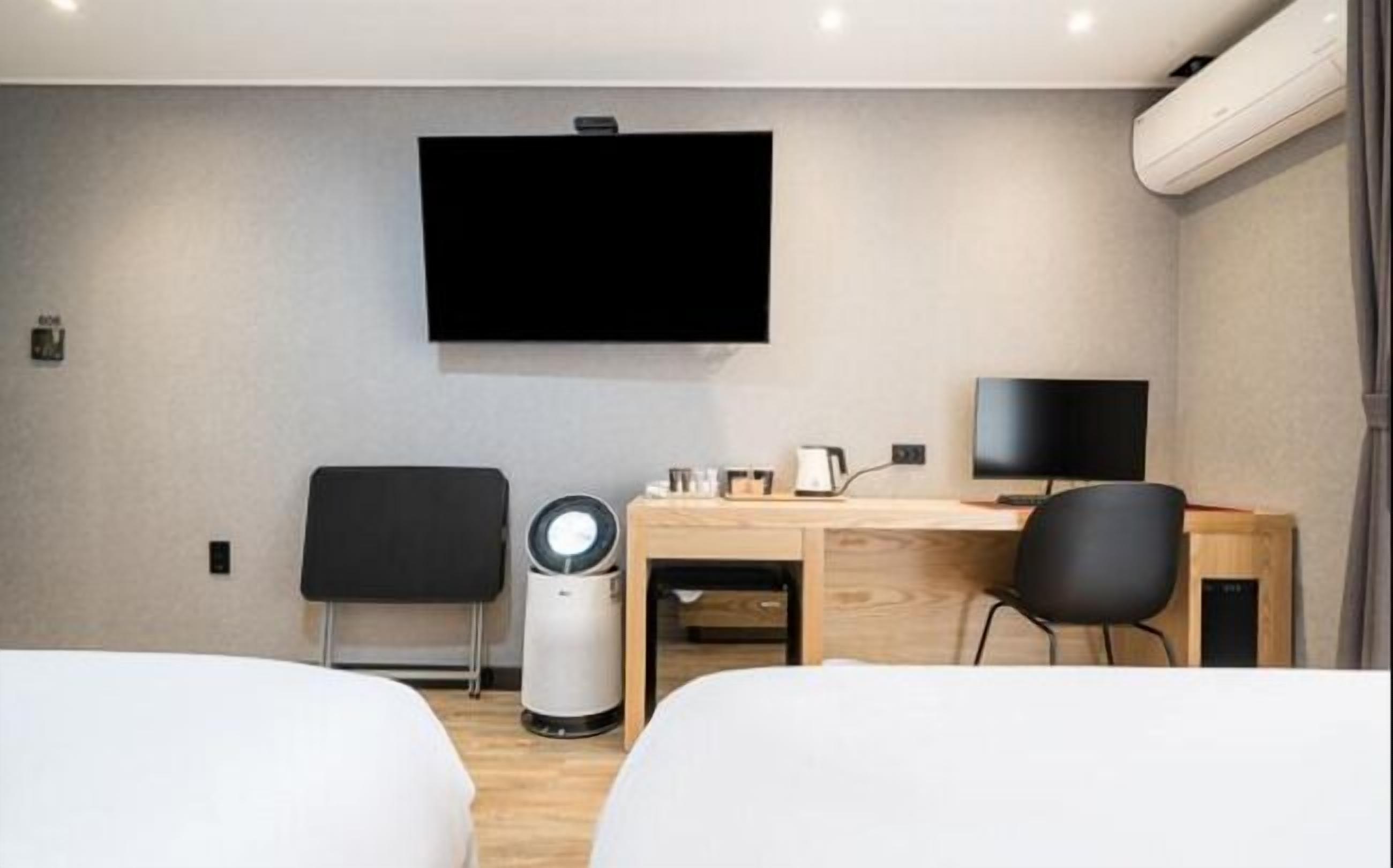A hotel room with a bed, a desk, a chair, a TV, and a trash bin.