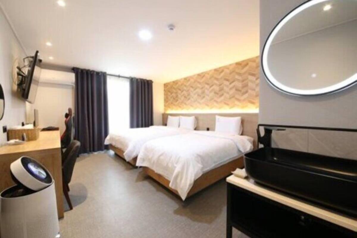 Una habitación de hotel con cama, escritorio, silla, espejo y una banca negra.