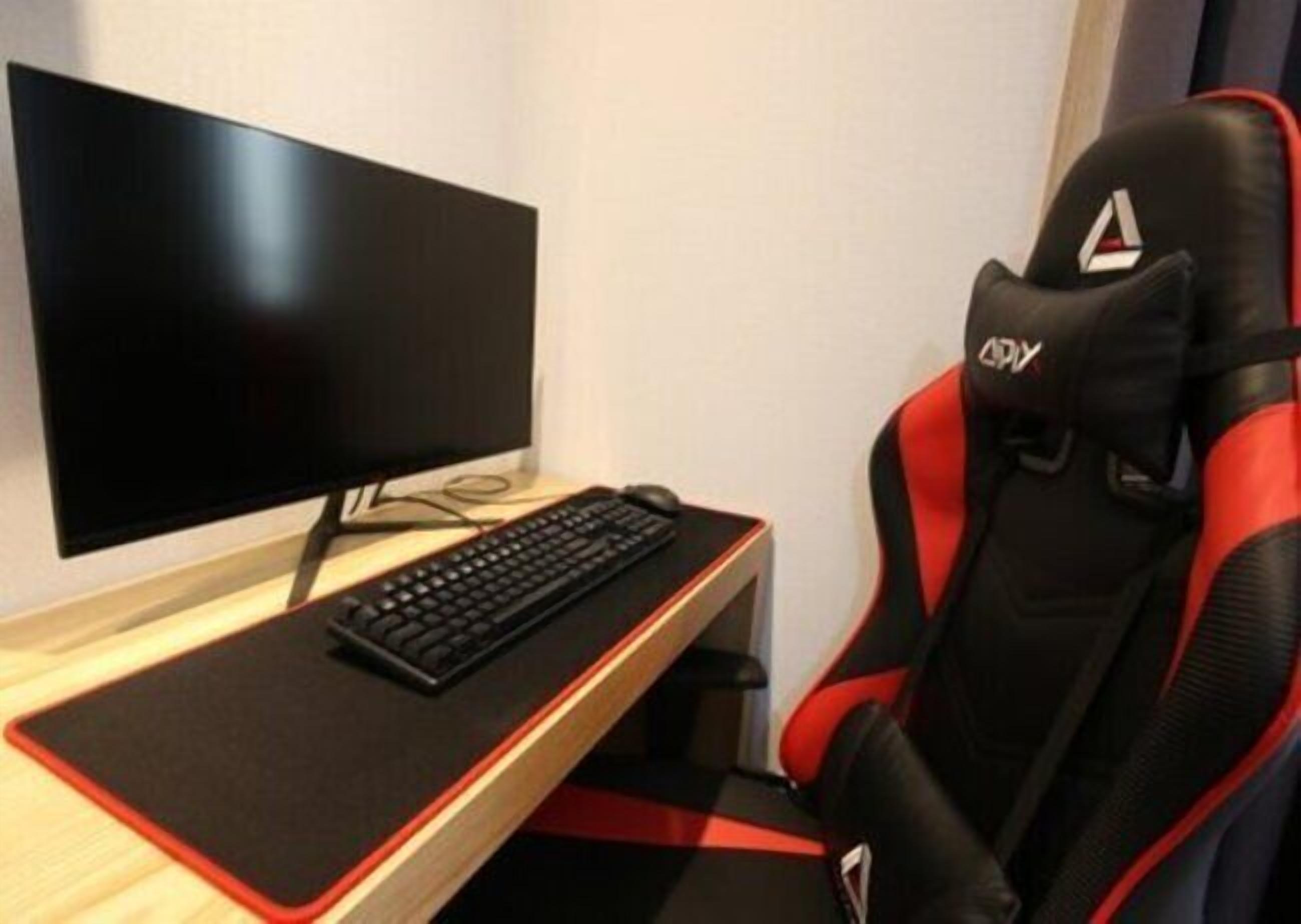 A gaming chair with red and black accents, a black keyboard, and a monitor on a desk.