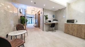 A modern hotel lobby with a reception desk, a seating area with a round table and chairs, and a hallway leading to the entrance. - LABE Hotel (Jeonju)