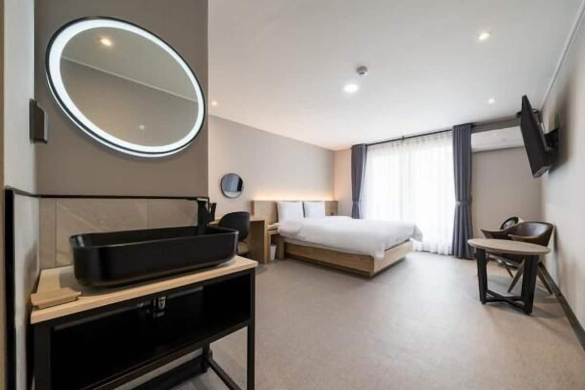 Una habitación de hotel moderna con una cama grande, un espejo redondo, un televisor de pantalla plana, una mesita pequeña y un escritorio con una computadora.