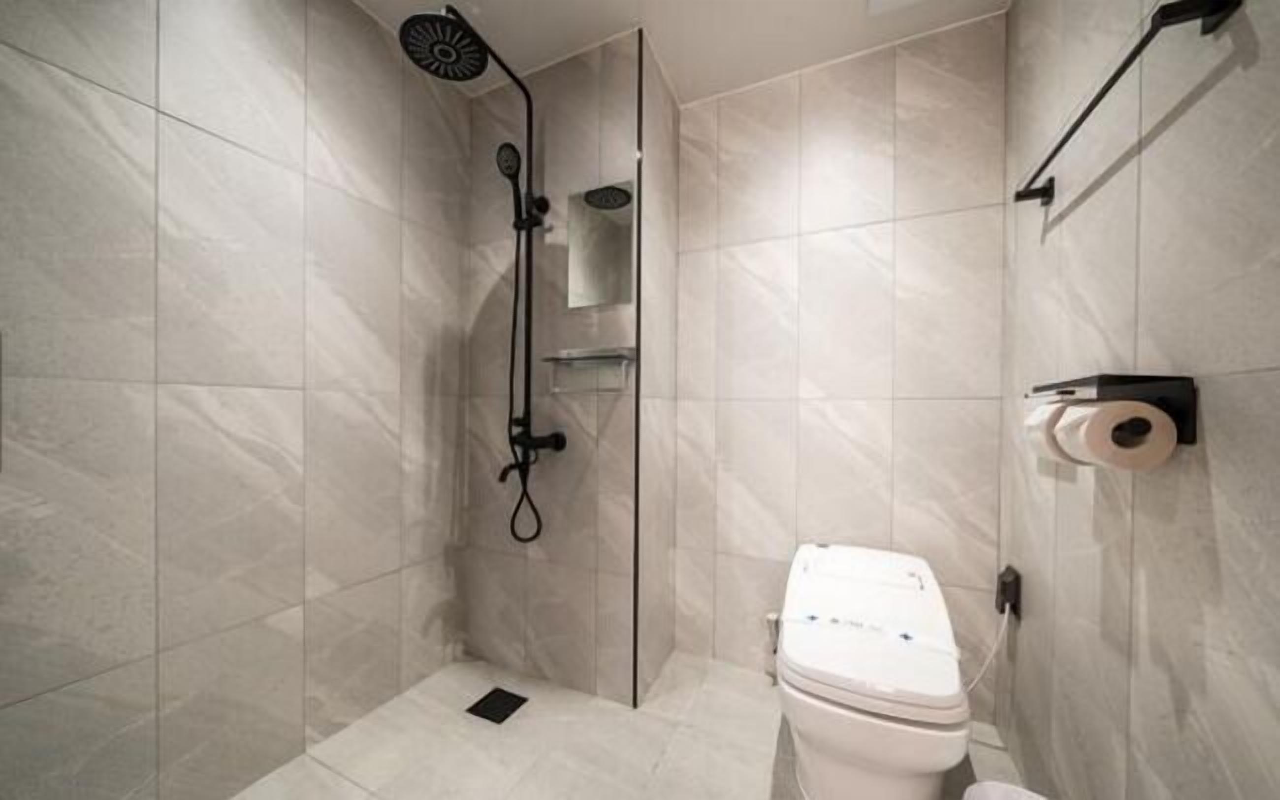 Un baño moderno con ducha envuelta en vidrio, inodoro y dispensador de toallas.