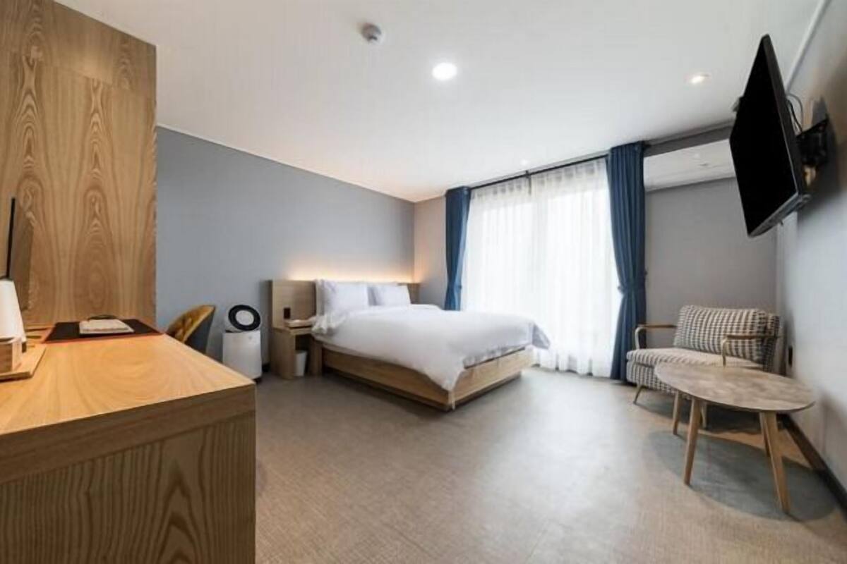 Habitación de hotel con escritorio de madera, una cama, una silla y un televisor montado en la pared.