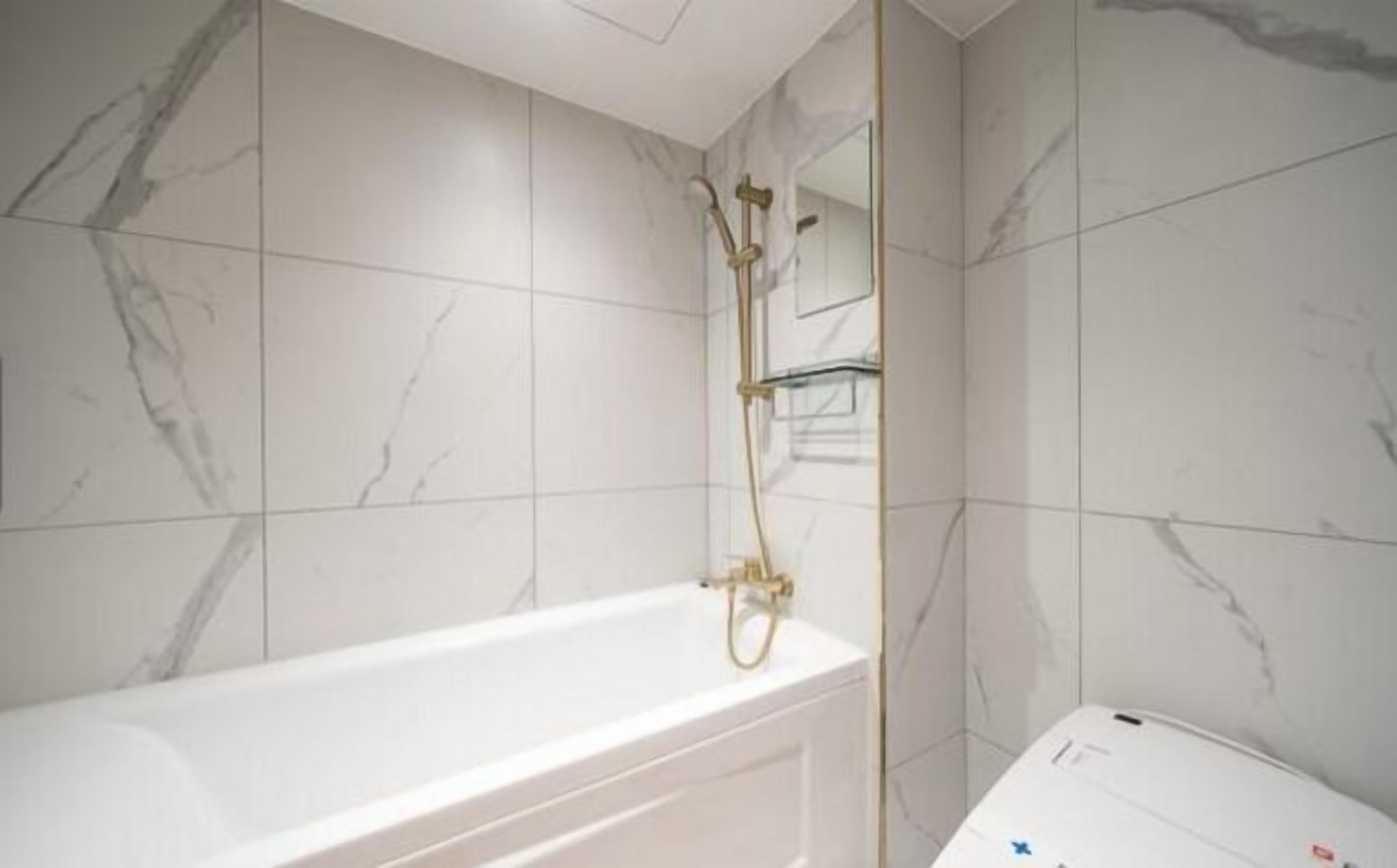 Un bagno con una vasca da bagno bianca, pareti in marmo e un accessorio doccia dorato.