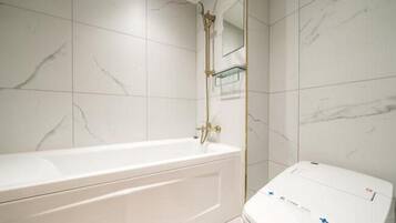 A bathroom with a white bathtub, a toilet, and a shower area.