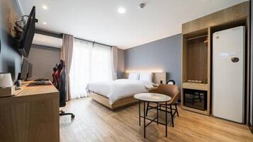 A modern hotel room with a bed, a desk, a chair, and a wardrobe.