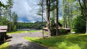A lodge with a paved driveway leading to a dock by a lake, surrounded by dense forest and a mountain in the background. - Cottages near Saratoga Springs (Lake Luzerne)