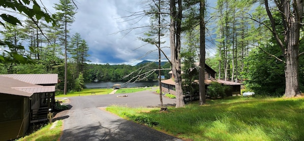 A lodge with a paved driveway leading to a dock by a lake, surrounded by dense forest and a mountain in the background.