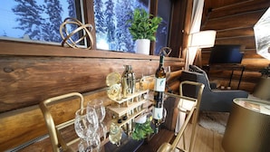 A wooden cabin interior with a bar area, a television, and a view of snow-covered trees through the window.