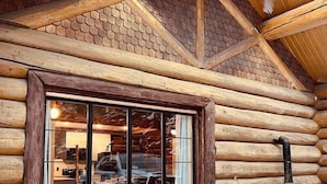 A log cabin with a large window reflecting a car and a building inside, a chimney, and a stone fireplace.