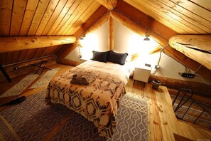 Un dormitorio acogedor en el ático, con cama, alfombra estampada y vigas de madera.