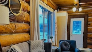 A log cabin interior with a sofa, armchair, ottoman, and a mirror on the wall.