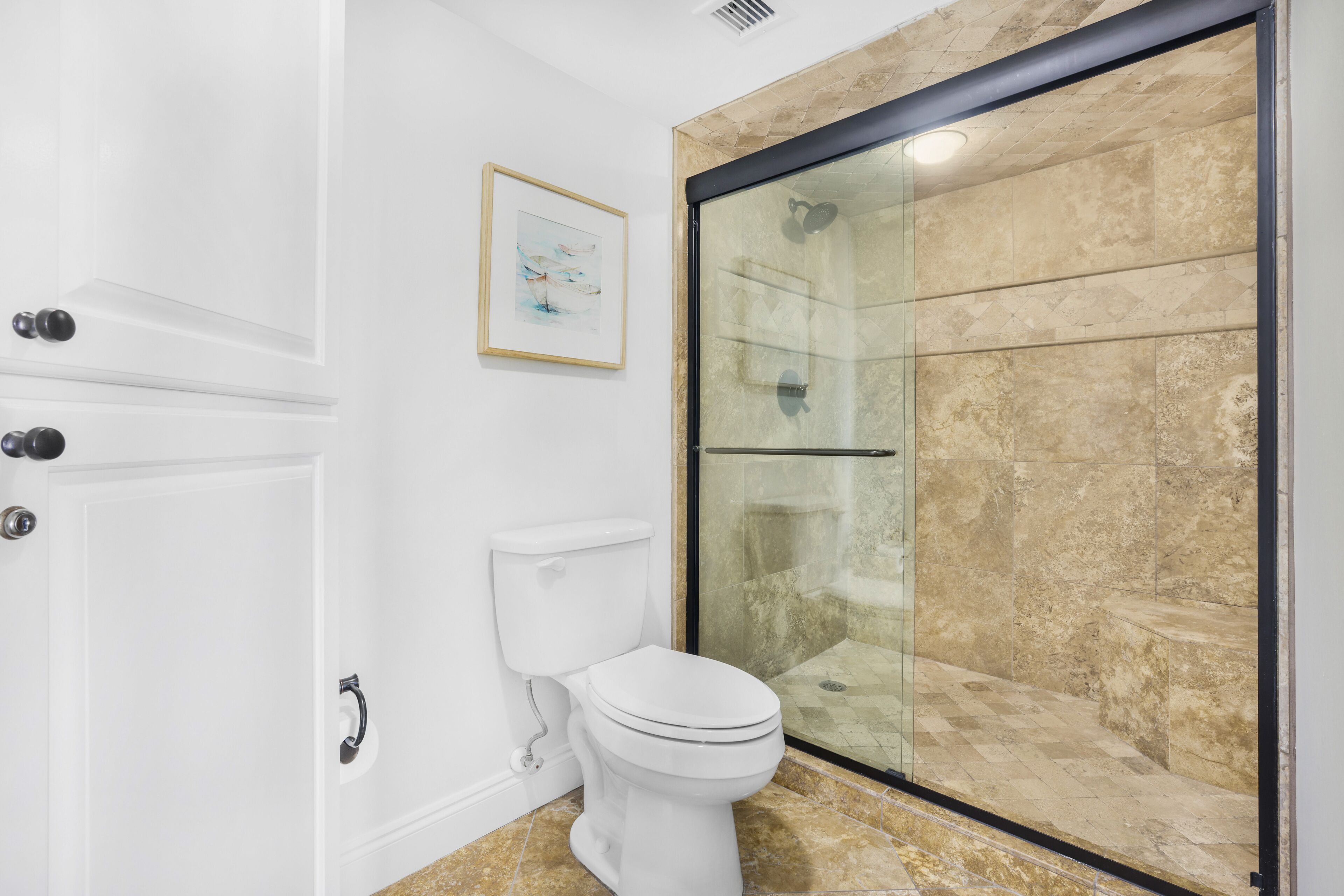 A bathroom with a glass-enclosed shower, a white toilet, and a framed picture on the wall.