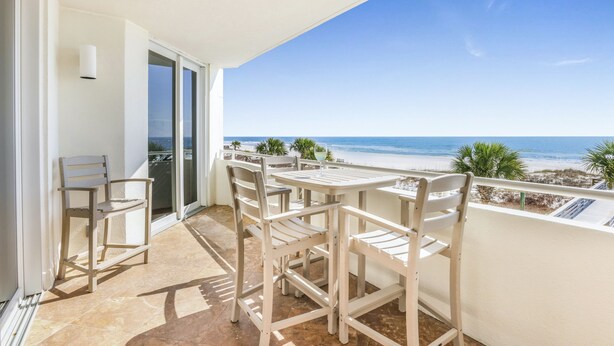 Ein Balkon mit Tisch und Stühlen mit Blick auf einen Strand.