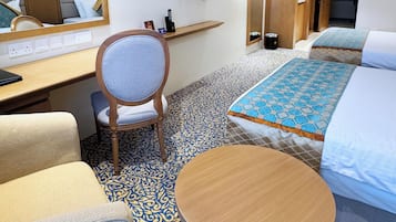 A hotel room with a bed, a desk, a chair, a round table, and a television on the wall.