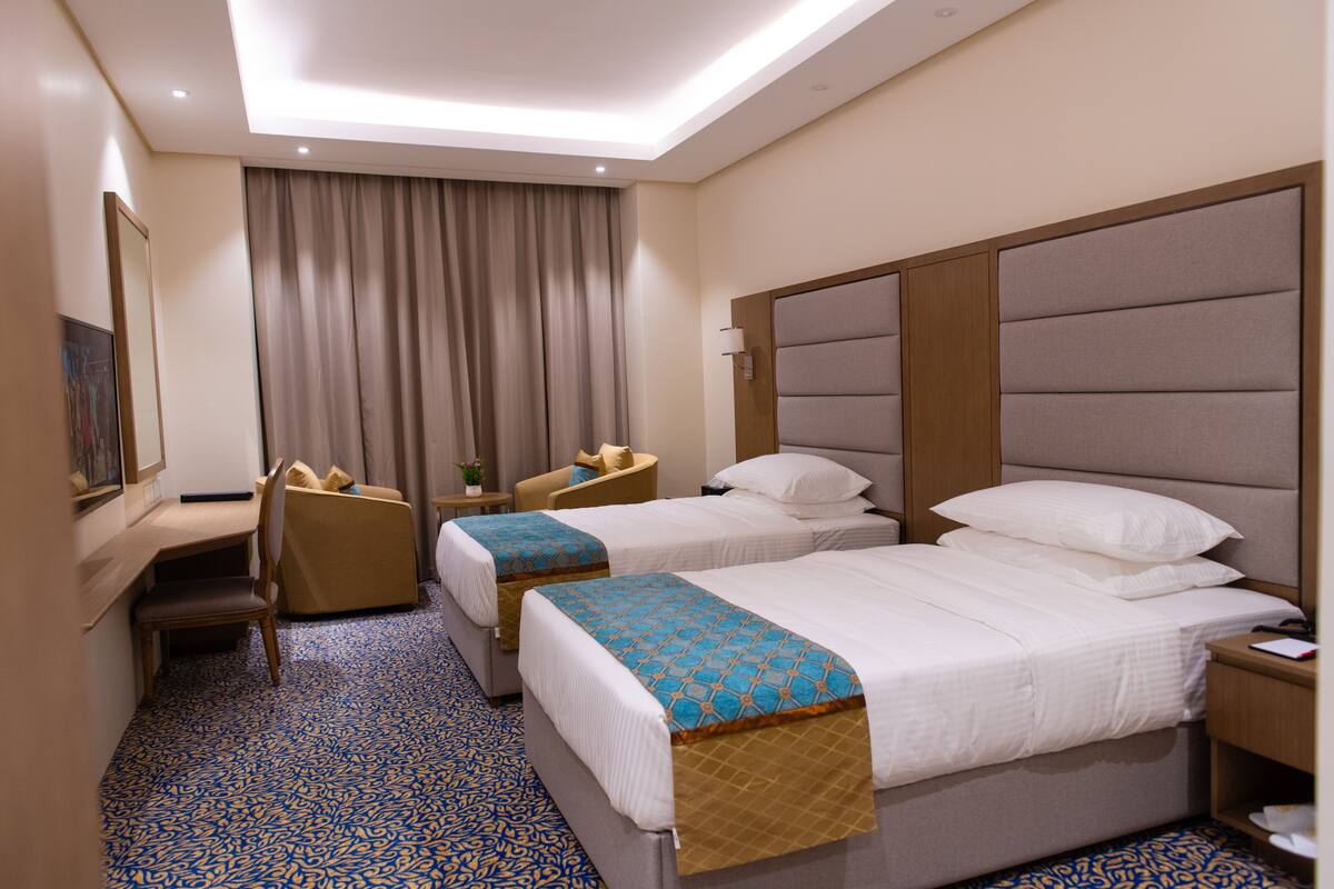 A hotel room with two beds, a desk, a chair, and a large window with curtains.