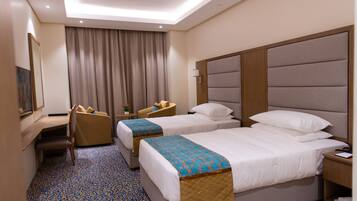A hotel room with two beds, a desk, a chair, and a large window with curtains.