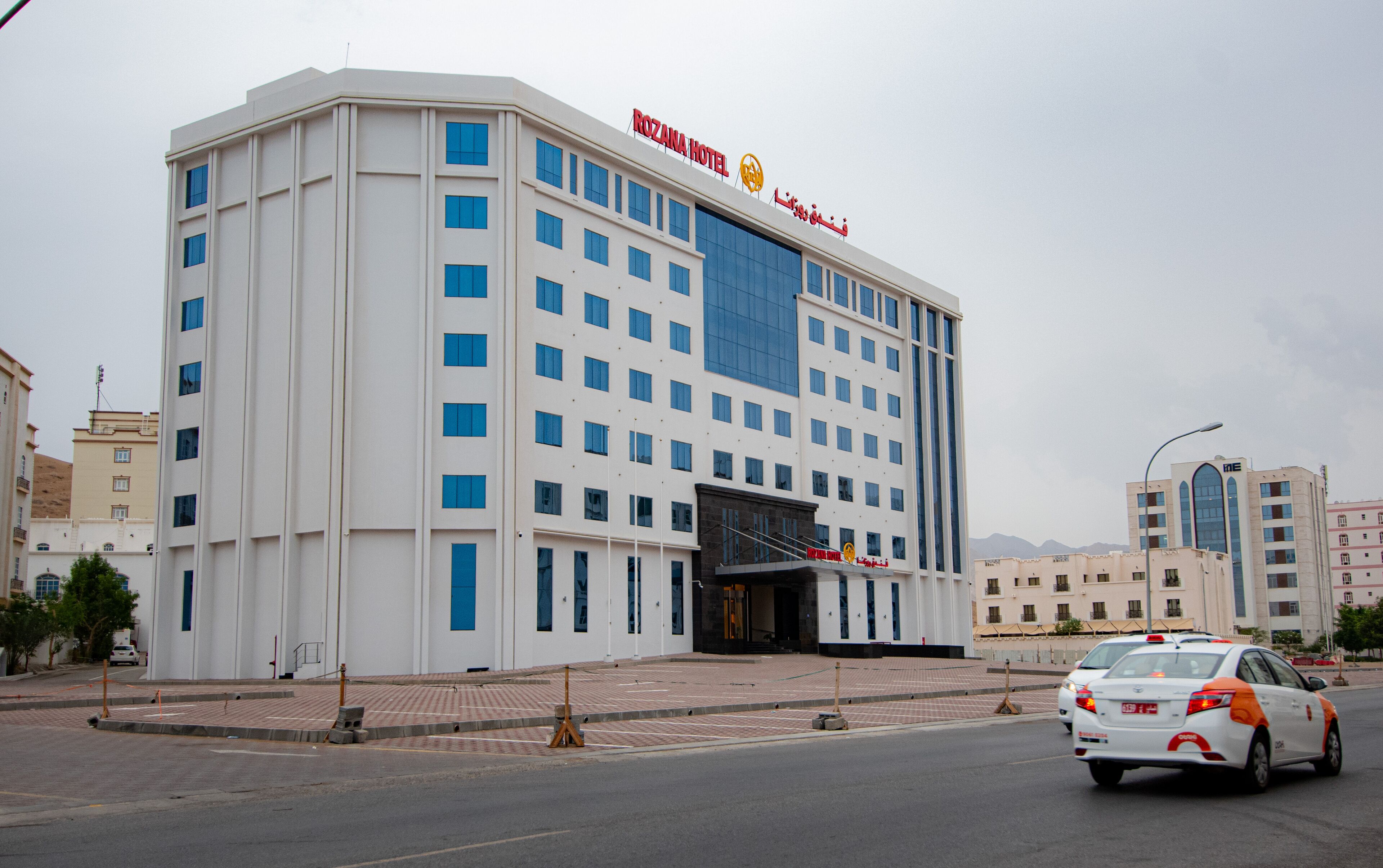 Un hôtel moderne, reconnaissable à son enseigne bien visible où l’on peut lire « ROZANA HOTEL ».