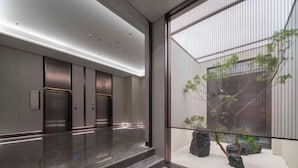 A modern elevator area with three elevators, a polished marble floor, and a view of a landscaped garden through a glass partition. - Anning Golden Age Hotel (Anning)