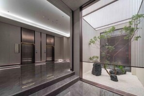 A modern elevator area with a reflective floor, a glass partition, and a view of a landscaped outdoor area with rocks and plants. - Anning Golden Age Hotel (Anning)