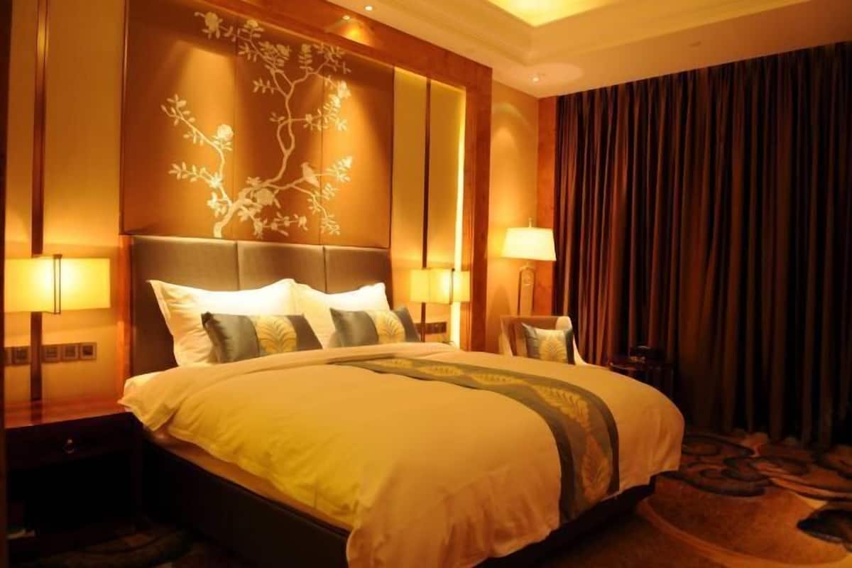 Habitación de hotel con una cama grande, dos mesitas de noche con lámparas, un panel decorativo en la pared y una cortina oscura.