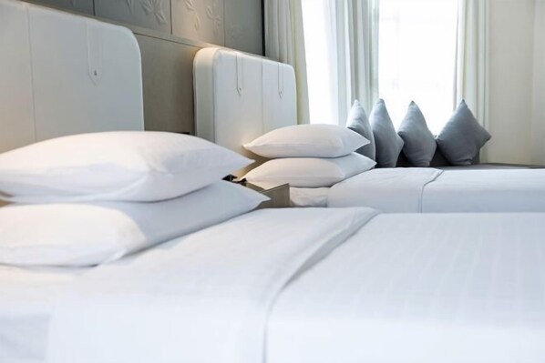 A hotel room with two beds, each with white bedding and multiple pillows.