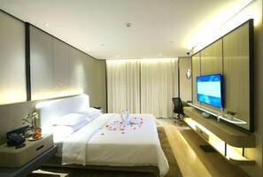 A modern hotel room with a large bed, a flat-screen TV, a bedside table with a lamp, and a large mirror. - Baijia Intercontinental Hotel (Jiujiang)