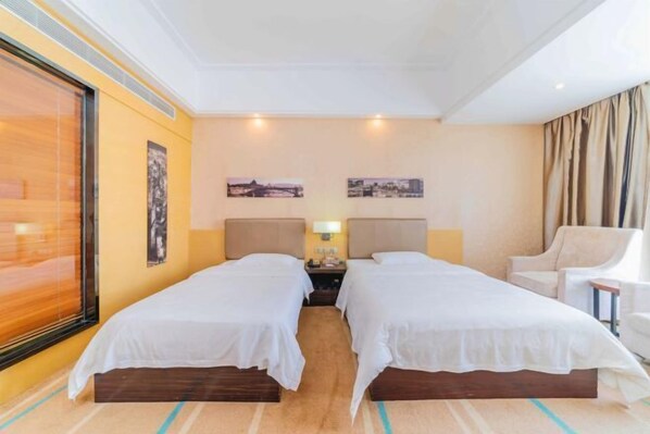A hotel room with two single beds, a nightstand with a lamp, a chair, and a large window with curtains.