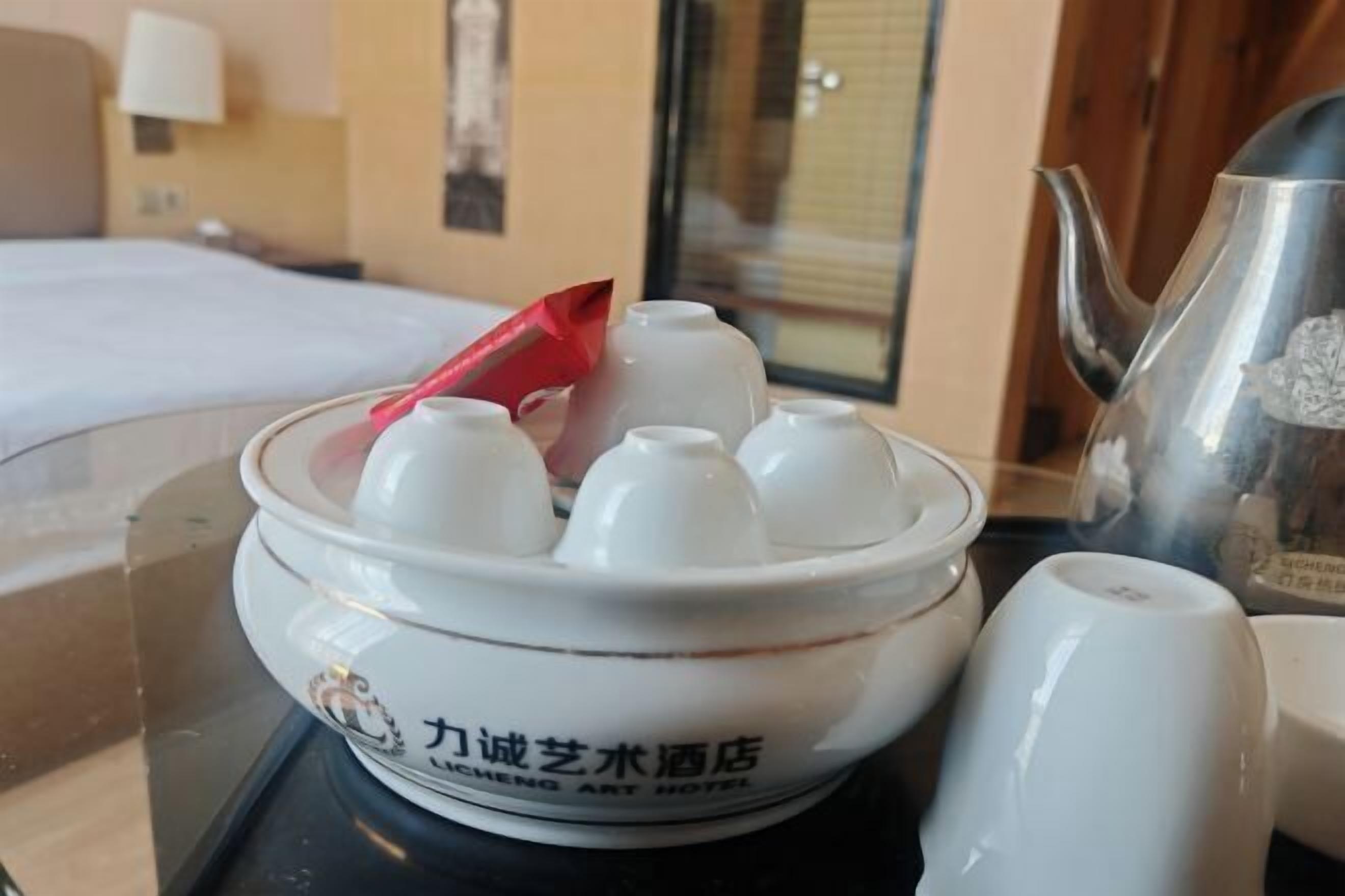 A hotel room with a bed, a table with a decorative bowl, a teapot, and a cup.