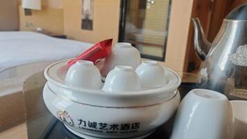 A hotel room with a bed, a table with a decorative bowl, a teapot, and a cup.