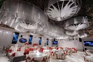A banquet hall with round tables, white tablecloths, and red floral arrangements. - Licheng Art Hotel (Raoping)