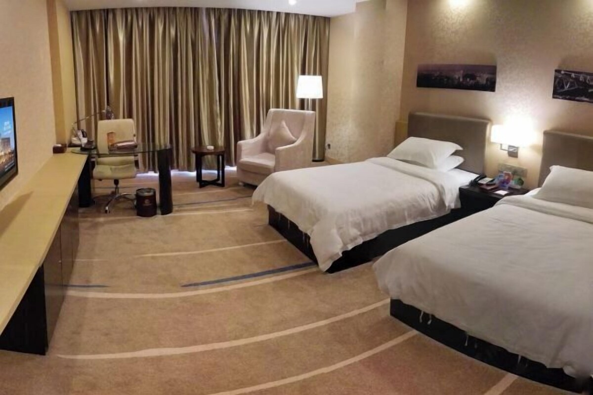 A hotel room with two beds, a desk, a chair, a lamp, and a TV.