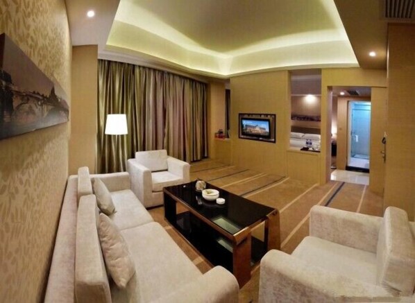 A hotel room with a sofa, armchairs, a coffee table, a TV, and a curtain.