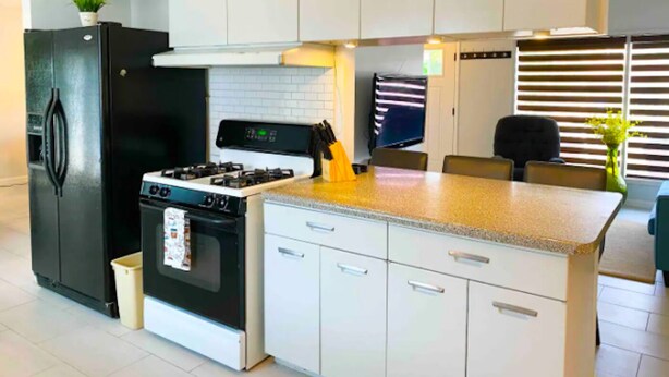 Una cocina moderna con gabinetes blancos, un refrigerador negro, una estufa y un comedor con mesa y sillas.