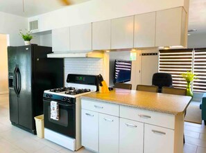 A modern kitchen with white cabinets, a black refrigerator, a stove, and a dining area with a table and chairs. - Beautiful New Family Home in West Side Of Town (El Paso)