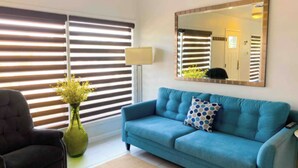 Una sala de estar con un sofá azul, un sillón negro, un jarrón verde con flores y un espejo grande en la pared.
