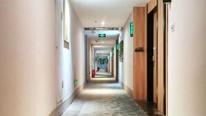 A long, narrow hotel corridor with a patterned carpet, wooden doors, and green exit signs.