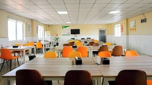 A conference room with multiple tables and chairs, a television on the wall, and a door on the right side.