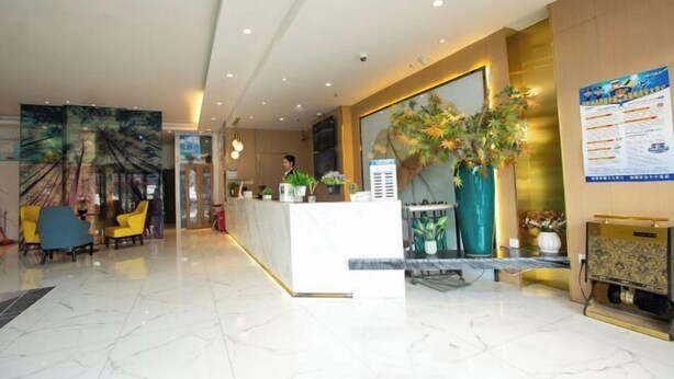 A hotel lobby with a reception desk, seating area, and decorative plants.