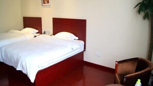 A hotel room with a double bed, a wooden headboard, a small table with a chair, and a potted plant.