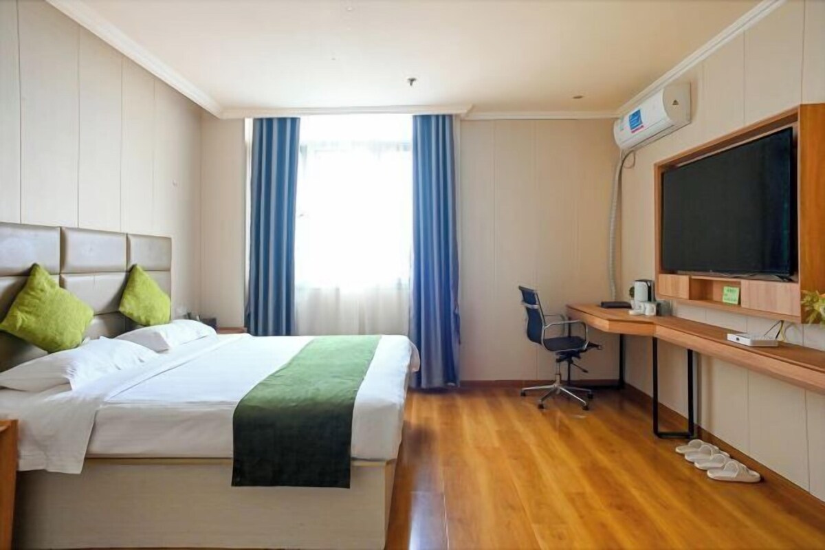 A hotel room with a bed, a desk, a chair, a television, and a window with curtains.