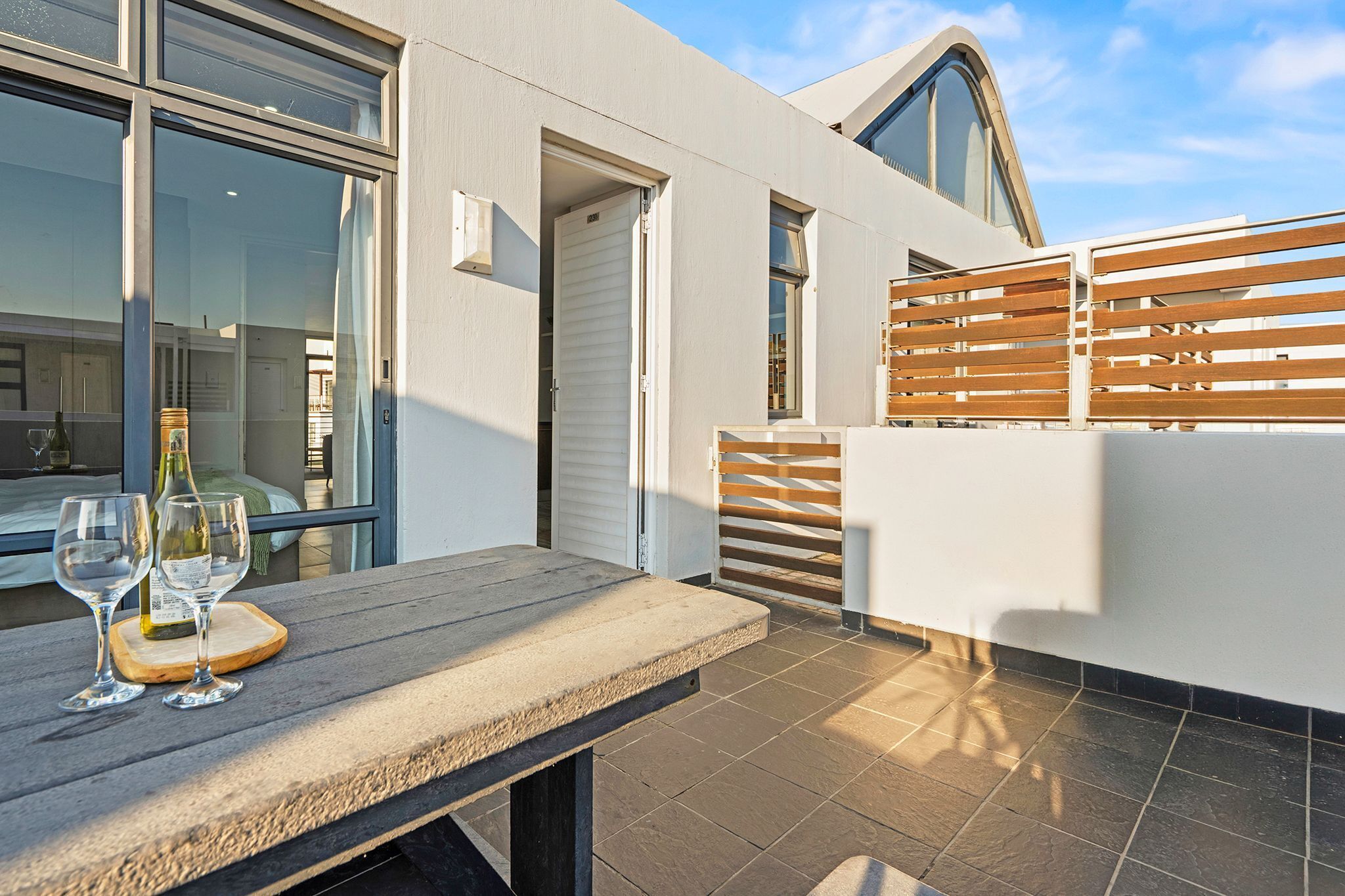 A modern outdoor patio with a table set for two, a wine bottle, and glasses.