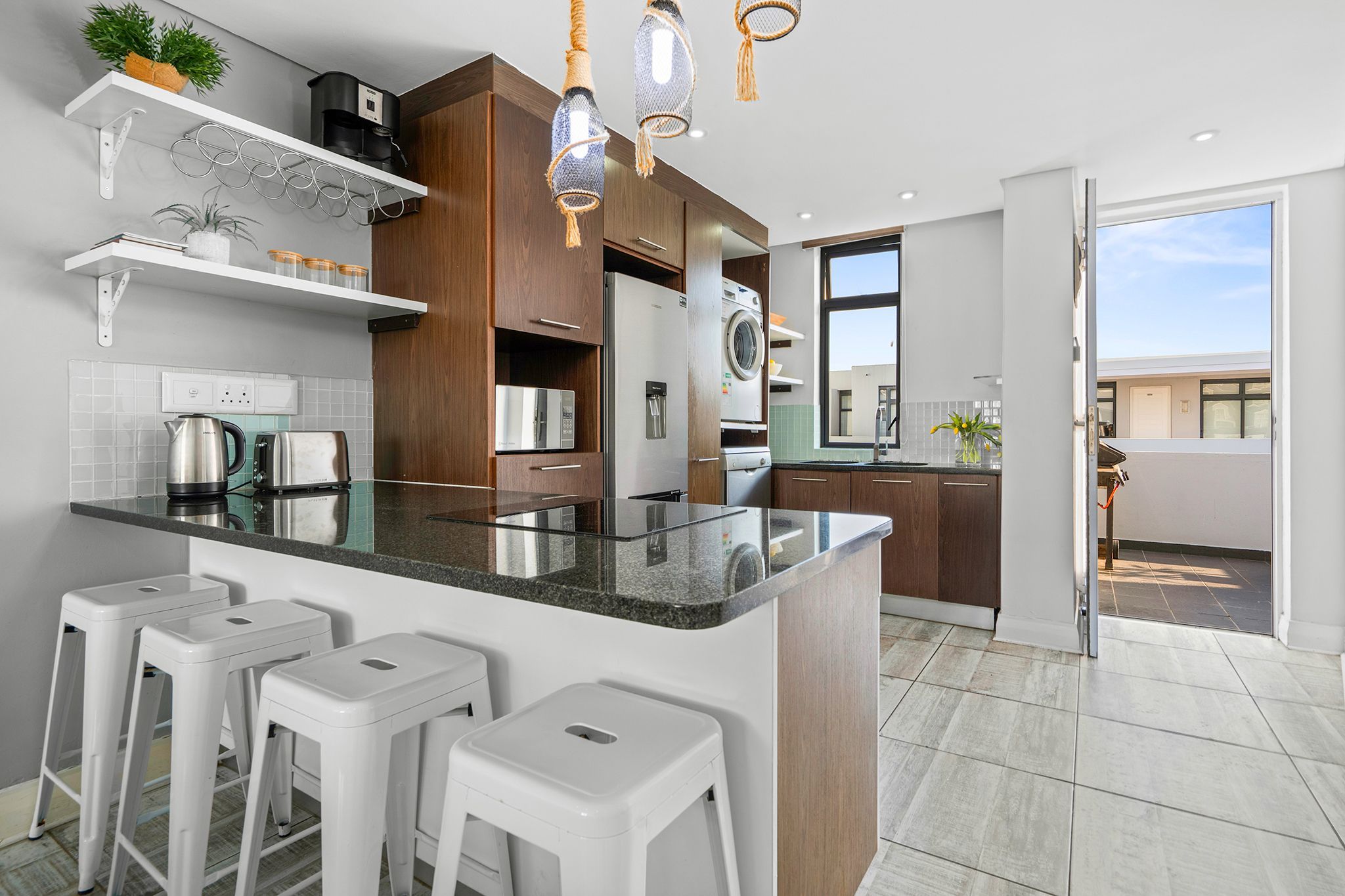 A modern kitchen with a central island, bar stools, and a view to the outside.