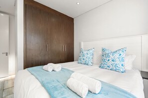 A modern bedroom with a large bed, white bedding, and blue floral pillows.