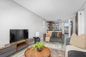 A modern living room with a flat-screen TV, a wooden coffee table, and a grey sofa. - Eden On the Bay 231 (Cape Town)