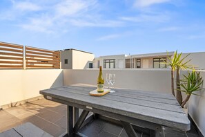 A rooftop terrace with a table, a bottle of wine, and two glasses. - Eden On the Bay 231 (Cape Town)